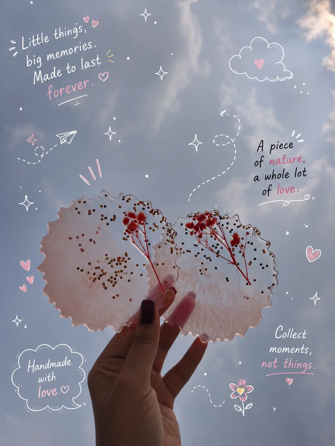 Pair of handmade blush resin pieces with pressed red flowers held against the sky
